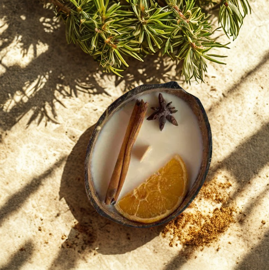 Duftkerze Coco Spice dekoriert mit Zimt und Orange in echter Kokosnussschale im Sand
